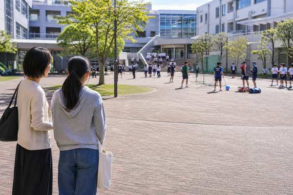 学校説明会で校庭にいる在校生の様子を並んで見学する保護者と中学生の写真