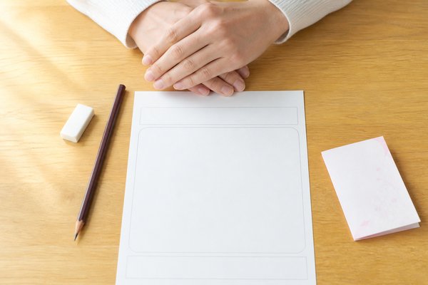 保護者が白紙のコメント用紙と鉛筆を前に、書く言葉を選んで手を止めている様子
