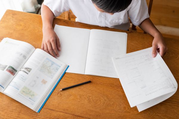 自宅の机で教科書と道徳ノート、返却されたワークシートを並べて見直す中学生