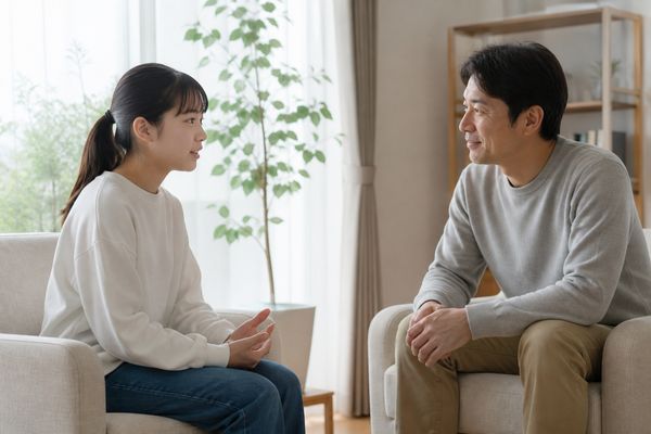 明るいリビングで向かい合って座り、中学3年生の娘が話すのを父親が静かに聞いている様子