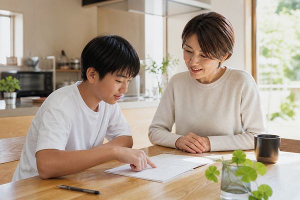 中学生と保護者が食卓で1週間の勉強計画の進み具合を一緒に振り返っている様子