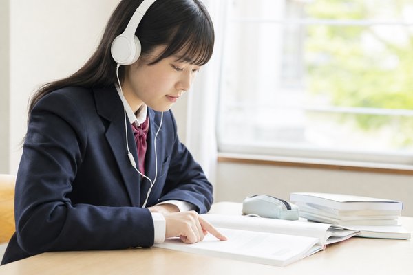 制服の高校生がヘッドホンで教科書音声を聞きながら英語の本文を目で追っている様子