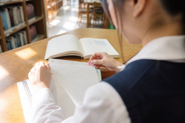 自習室で高校生が授業ノートの分からない箇所へはてなマークの付箋を貼り、その日のうちに調べようとしている様子