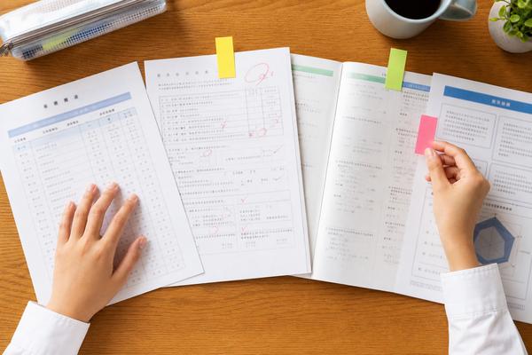 通知表・返却された答案・ワーク・評価資料を机に並べ、付箋を貼りながら見比べている中学生の手元