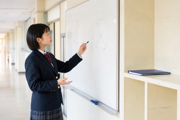 制服の高校生がホワイトボードに書いた図形の問題を指しながら、自分の解法の方針を言葉で説明している様子
