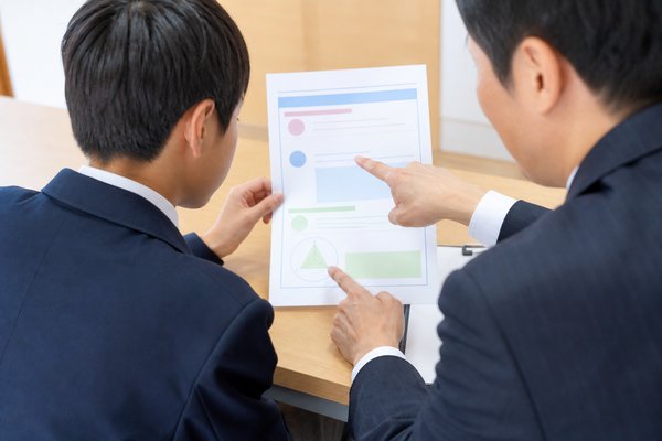 面談室で講師と一緒に模試の成績表を三か所に分けて確認する男子中学生