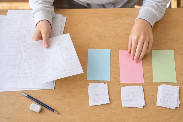 机の上でテストの答案を広げ、間違えた原因ごとに色分けした付箋へ仕分けしている手元