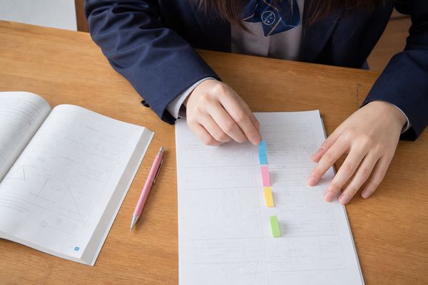 制服姿の高校生が、解き終えた答案に4色の付箋を貼り分けて失点の原因を整理している手元