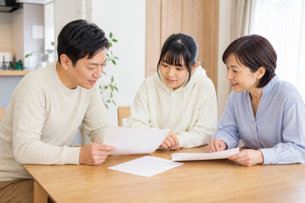 両親と中学生の子どもが明るい食卓で成績表と学校の案内を一緒に確認している様子
