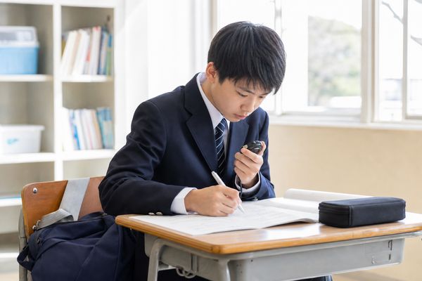 制服の男子中学生がストップウォッチで時間を測りながら例題を解いている様子