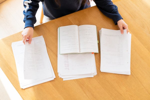 自宅のダイニングテーブルで、返却されたテストとワークを3つの山に分けて整理する中学生の手元