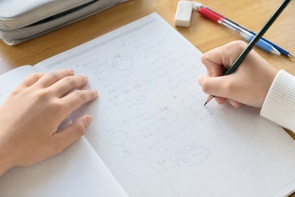 中学生が数学のワークの間違いを色を分けて直し、途中の考え方を書き足している手元の接写