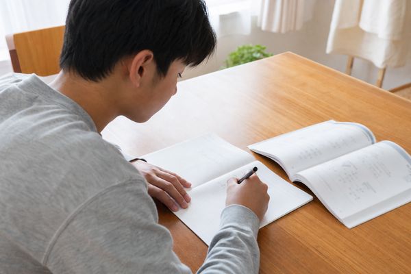 私服の中学生が自宅の机で、短い計算練習を一問ずつ落ち着いて解いている様子