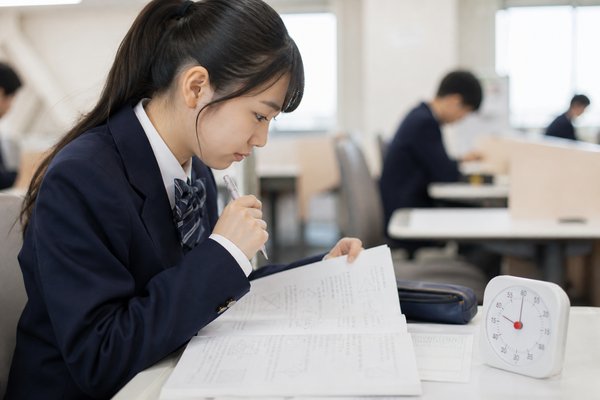 制服姿の高校生が自習室でタイマーを置き、二次試験の過去問を時間を計って解いている様子