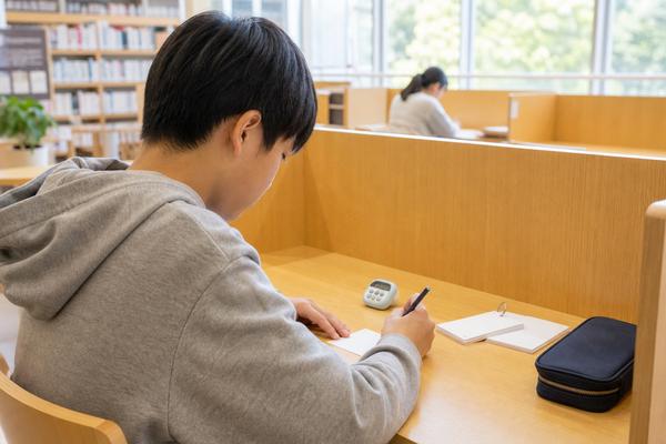 図書館の自習席で、タイマーを置いた中学生が返却された答案を見ながら解き直しに取り組んでいる様子