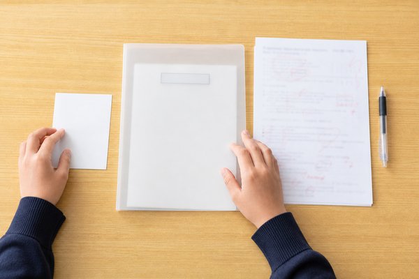 中学生が机の上で一枚メモ・通知表を入れたクリアファイル・採点済みの答案を並べて整理している手元