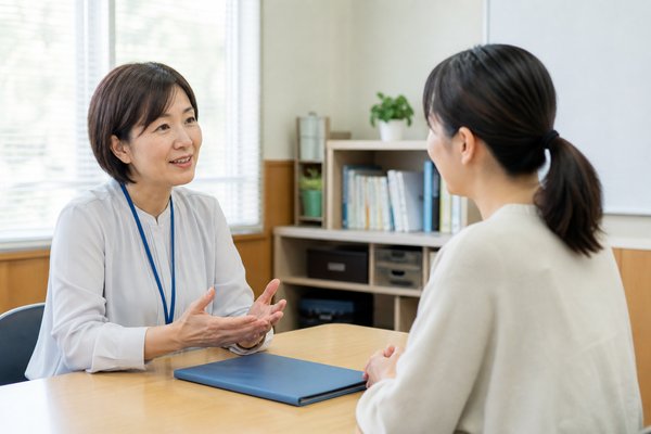 学校の明るい面談室で、先生と保護者が資料を挟んで落ち着いて相談している様子