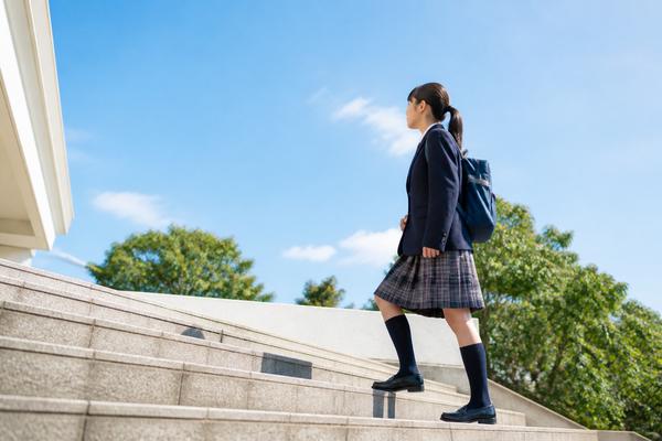 青空の下、制服姿の中学生が階段を一段ずつ上がって前へ進んでいく様子