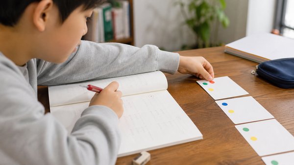 自宅で間違えた問題を赤ペンで解き直し次の行動カードに手を伸ばす中学生