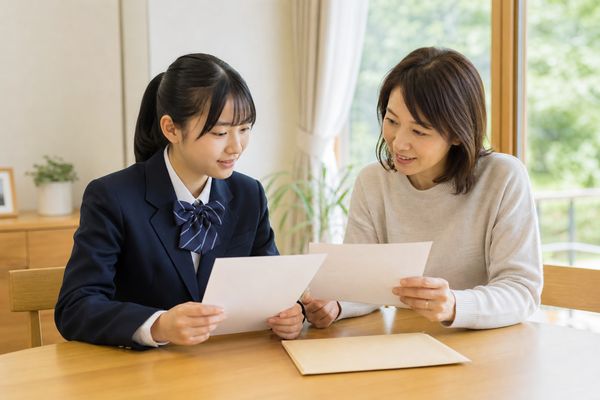 明るいダイニングで制服の高校生と保護者が募集要項と高校の案内書類を並べて確認している様子