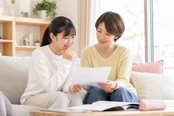 私服の中学生の娘と母親がソファに並んで座り、成績表を見ながら次にできることを一緒に話している様子