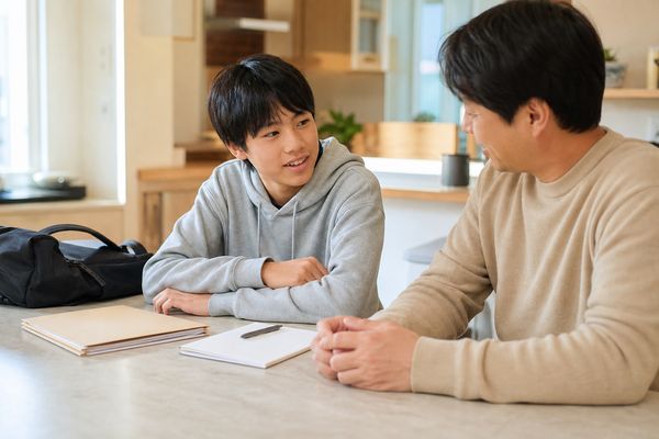 中学生が自宅のキッチンカウンターで保護者とテストの振り返りを話している様子