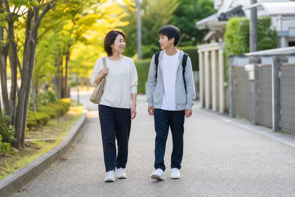 並んで歩きながら穏やかに話す母親と中学生の息子の写真