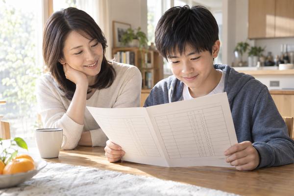 明るいダイニングで通知表を一緒に見る中学生と保護者