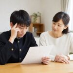 答案を見つめる中3の男子生徒と、隣で静かに見守る母親
