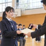 体育館の表彰式で賞状とメダルを受け取る高校生