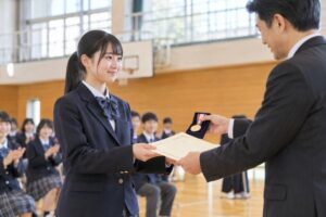 体育館の表彰式で賞状とメダルを受け取る高校生