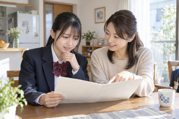 自宅のダイニングで、制服姿の高校生と母親が高校の通知表を開いて見ている場面