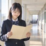 明るい校舎の廊下で、制服姿の中学生が通知表を開いて評定を確かめている場面