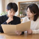 自宅のダイニングで、学生服姿の中学生と母親が通知表を一緒に開いて見ている様子