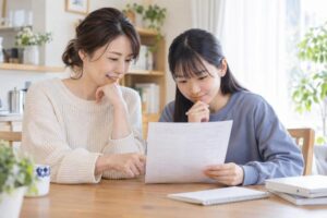 ダイニングテーブルで母親と中学生の娘が返却された答案を一緒にのぞき込みながら穏やかに話している様子