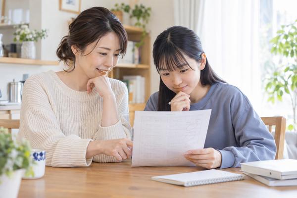 ダイニングテーブルで母親と中学生の娘が返却された答案を一緒にのぞき込みながら穏やかに話している様子