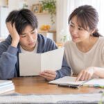 自宅のダイニングで、オール2の通知表を見て困った表情の中学生に保護者が寄り添って話している様子