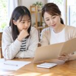 自宅のテーブルで母と中学生の娘が通知表を一緒に確認している