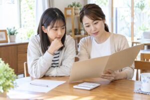 自宅のテーブルで母と中学生の娘が通知表を一緒に確認している