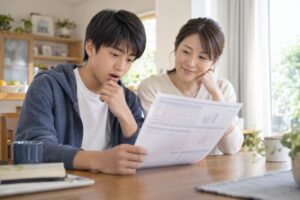 実力テストの成績票を見て考える中学生と、横で見守る母親