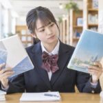 図書館で2冊の英語の教材を見比べ、どちらを使うか考える制服姿の高校生