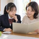 通知表と電卓を前に中学の内申点を一緒に確認する母親と中学生