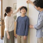 玄関の壁で中学生の息子の身長をメジャーで測る父親と母親