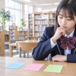制服の中学生が明るい学校の図書室で、色の違う三枚のカードを見比べて考えている様子。中学生共通テストと呼ばれる三つの試験を分けて選ぶことを表したアイキャッチ