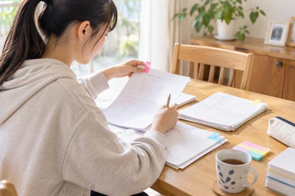 自宅のテーブルで返却された実力テストの答案を見直し、ピンクの付箋を貼っている中学生