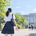 夏の日差しの中、模試の資料を手に校門へ向かって歩いていく制服姿の高校3年生