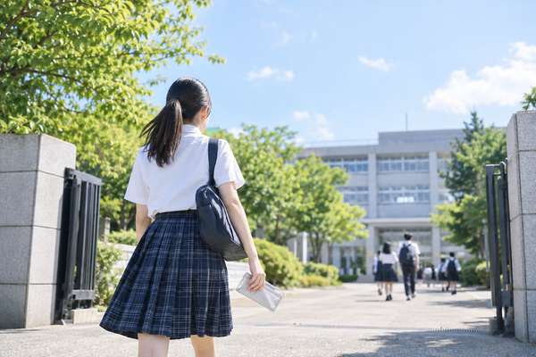 夏の日差しの中、模試の資料を手に校門へ向かって歩いていく制服姿の高校3年生