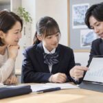 塾の面談席で、保護者と制服姿の生徒が、塾スタッフの示すタブレットの成績推移グラフを一緒に見ている様子