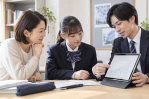 塾の面談席で、保護者と制服姿の生徒が、塾スタッフの示すタブレットの成績推移グラフを一緒に見ている様子