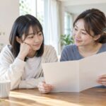 明るいリビングのテーブルで、中学生と母親が通知表を開いて一緒に見ながら、5段階評価の内容を話し合っている様子